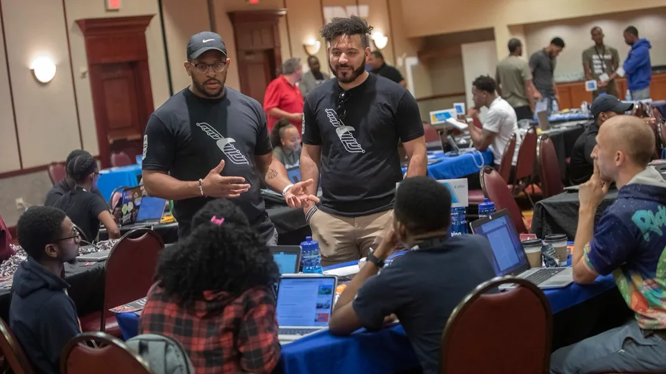 Tre Stewart and a colleague facilitating a hands-on American Airlines workshop with attendees around laptops