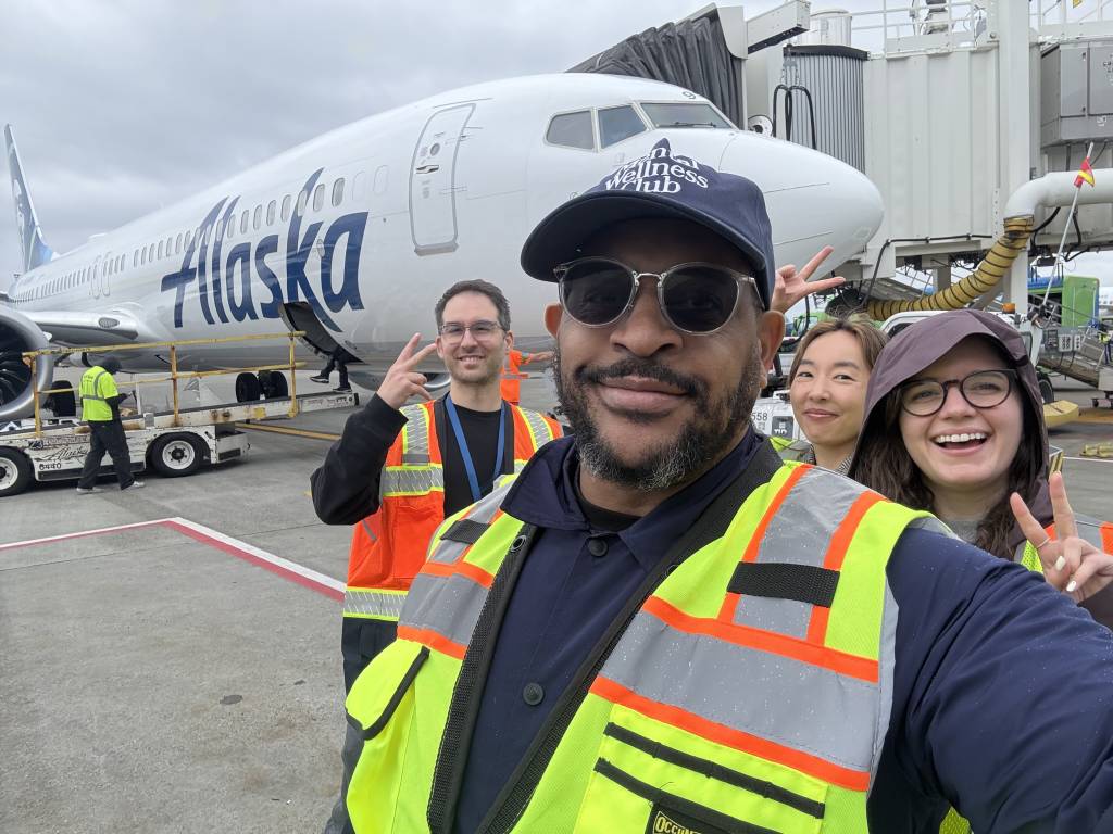 Tre in front of an Alaska Airlines aircraft smiling with a man and two women wearing safety vests.